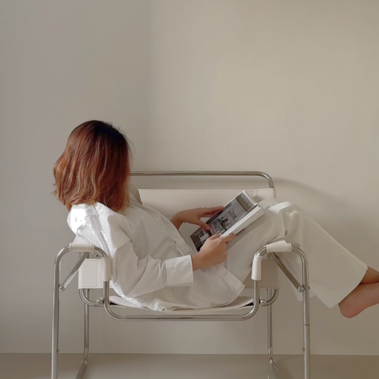 A woman in relaxed neutral-toned loungewear sits comfortably in a modern chair, reading a magazine in a sunlit room. The vibe is calm, thoughtful, and quietly confident—perfectly reflecting a mindful, sustainable approach to digital marketing.