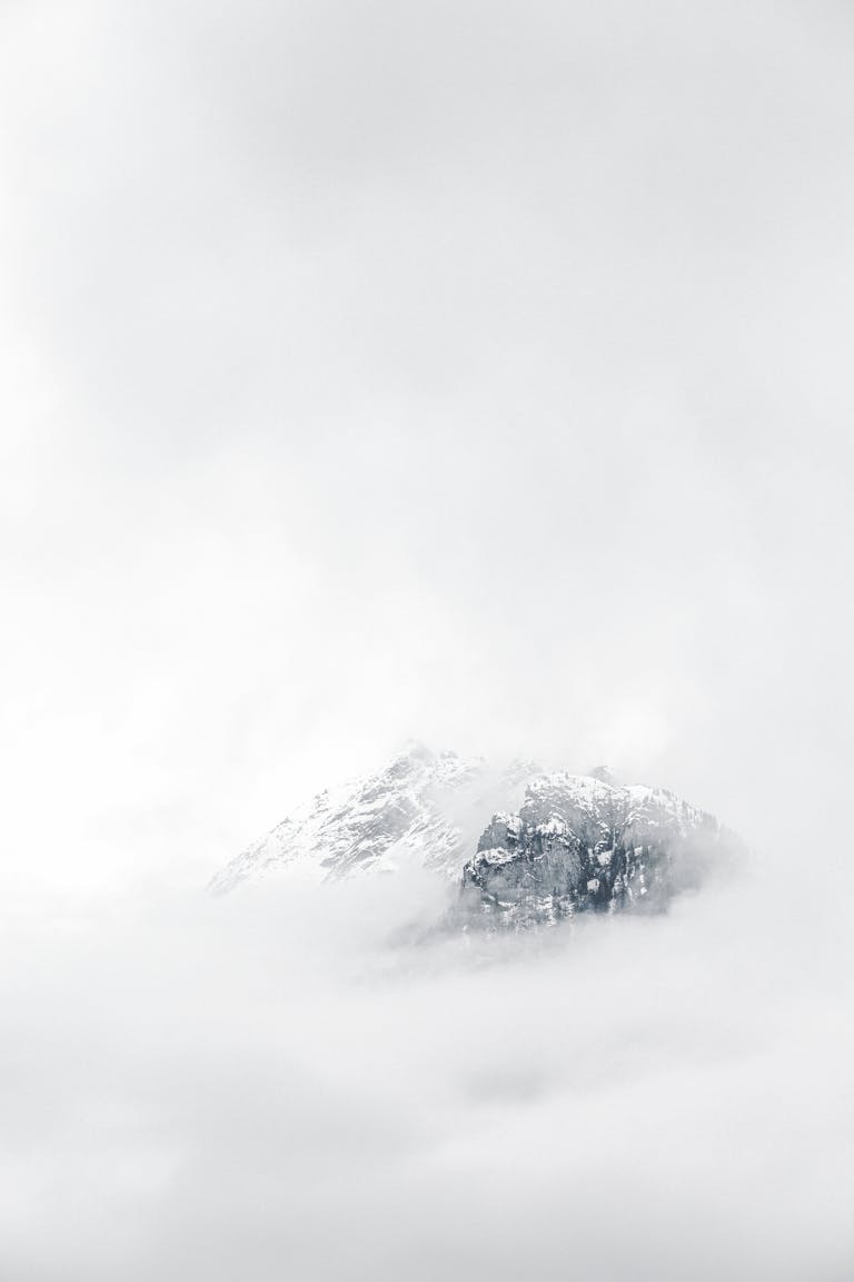 A minimal snowy mountain peak emerging from soft fog, symbolizing clarity, calm, and steady growth. Evokes the emotional tone of staying grounded in your content journey—even through uncertainty.