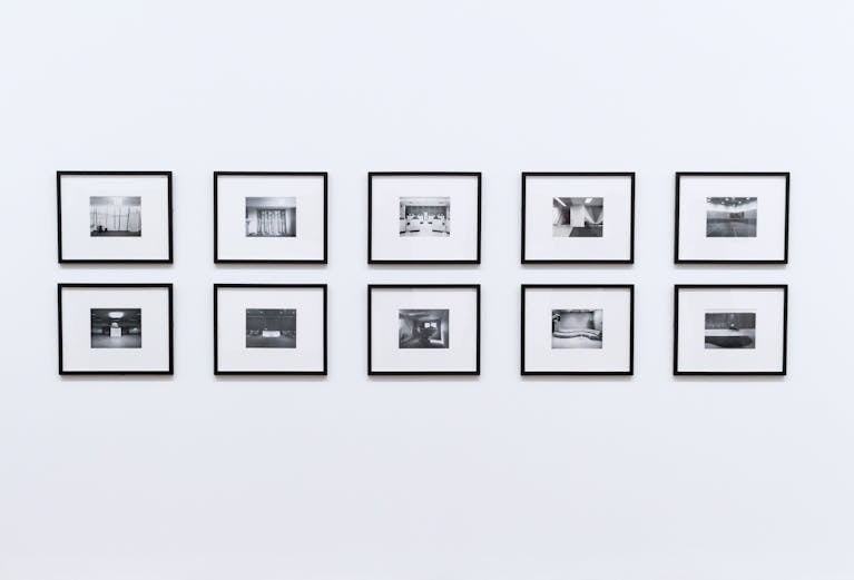 Minimalist photo wall featuring ten black-and-white framed pictures in two neat rows—symbolizing structure, repetition, and the quiet rhythm of intentional creativity.