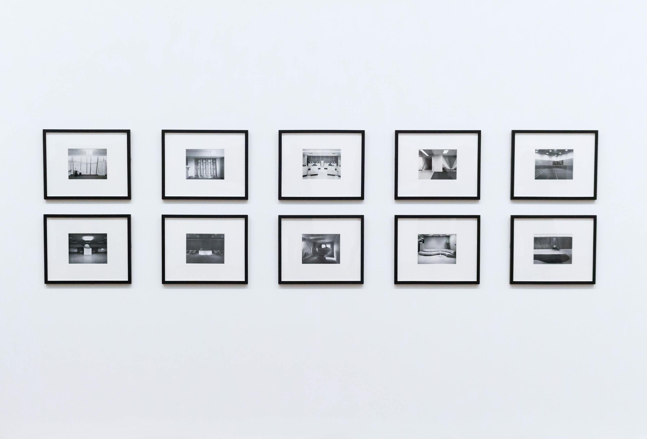 Minimalist photo wall featuring ten black-and-white framed pictures in two neat rows—symbolizing structure, repetition, and the quiet rhythm of intentional creativity.