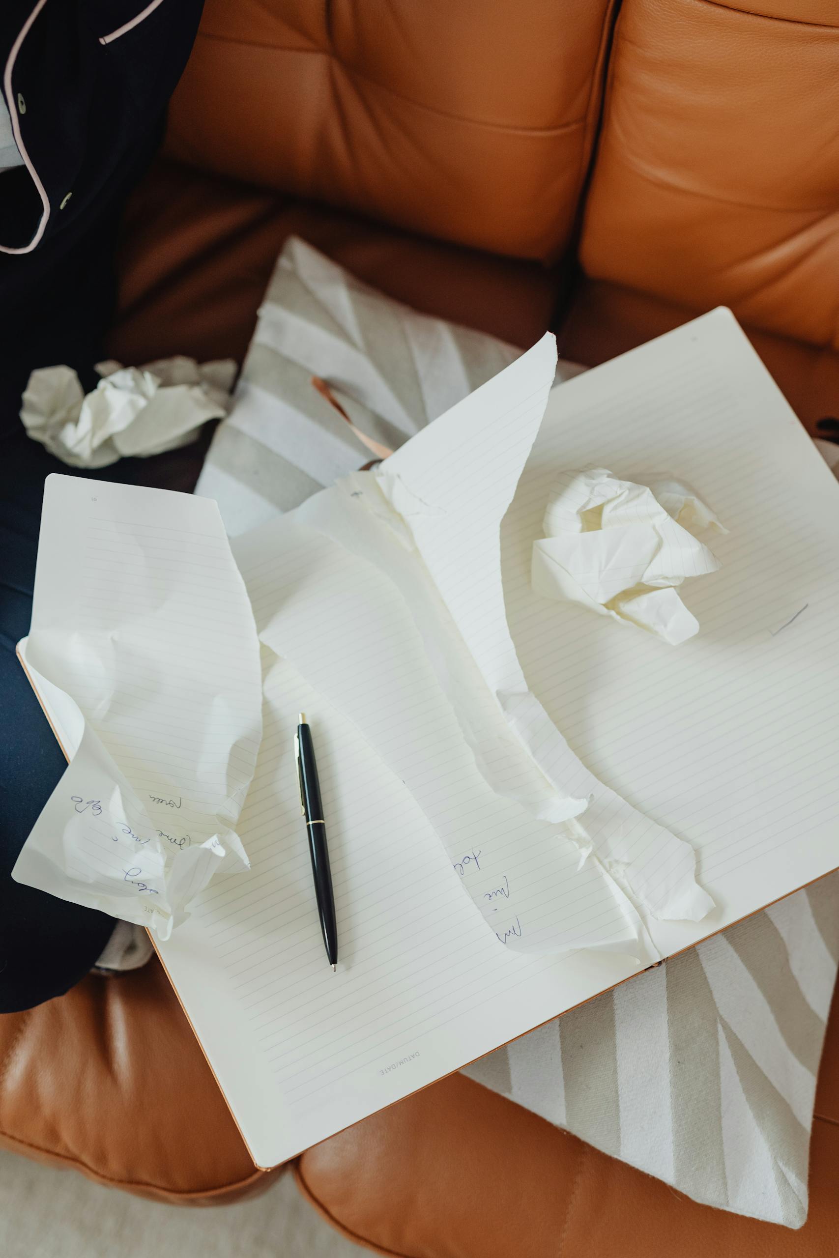 Torn papers and a pen scattered on an open notebook in a cozy indoor setting.