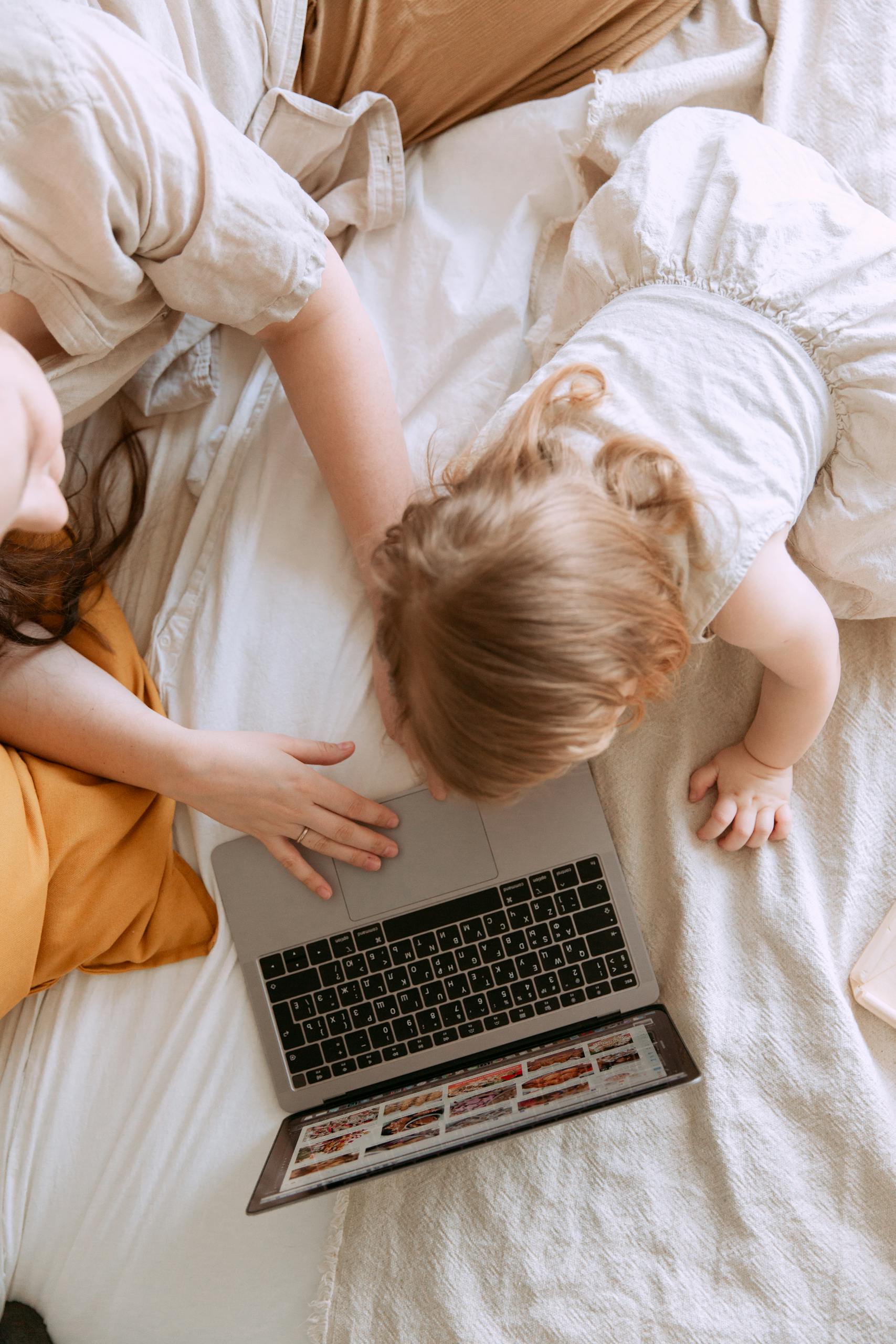A mother and child comfortably using a laptop on a cozy bed, enjoying shared screen time.