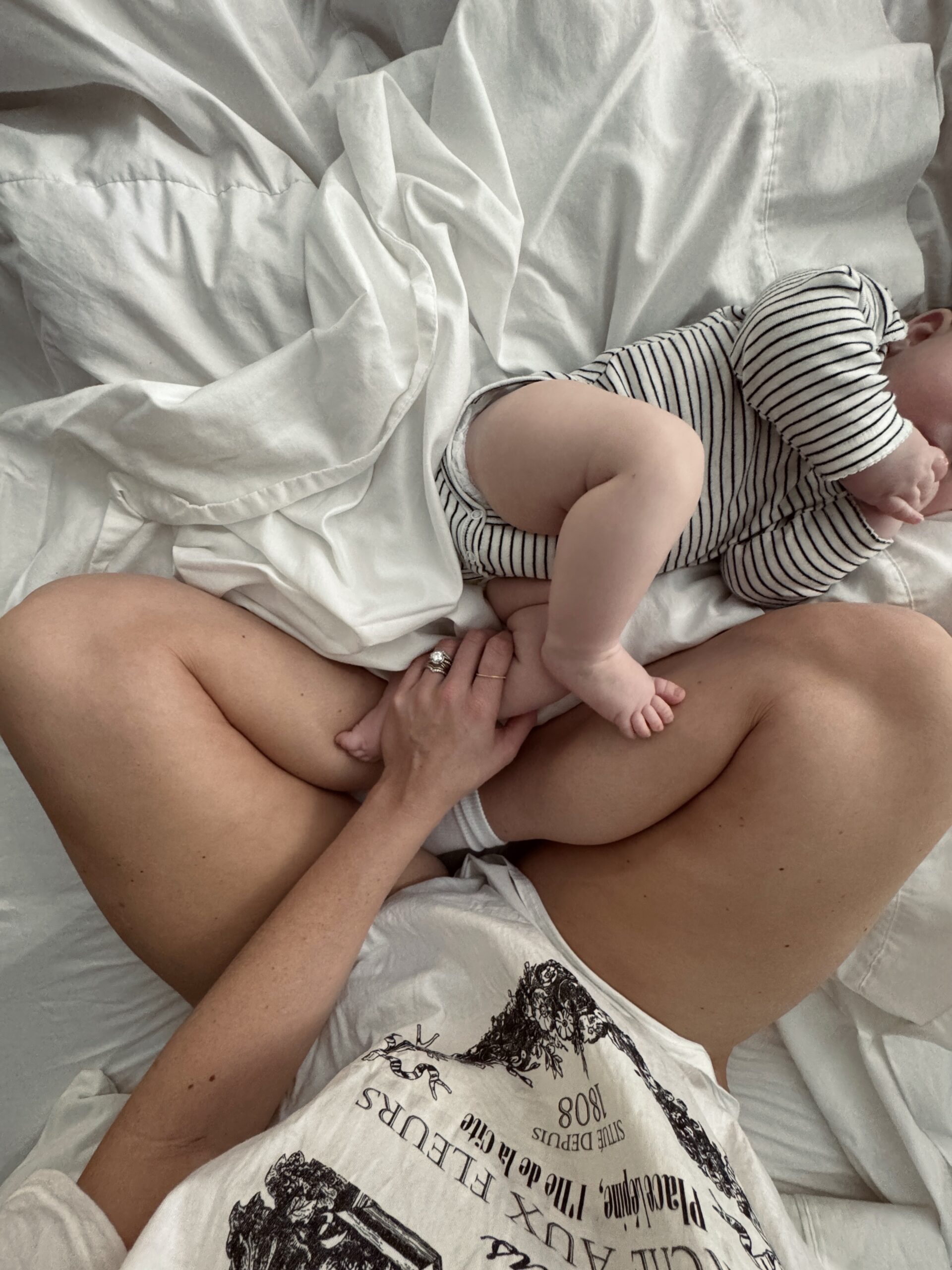 Mother sitting cross-legged on a bed holding her baby, symbolizing the reality of building a digital business during early motherhood and choosing a sustainable path that fits real life.