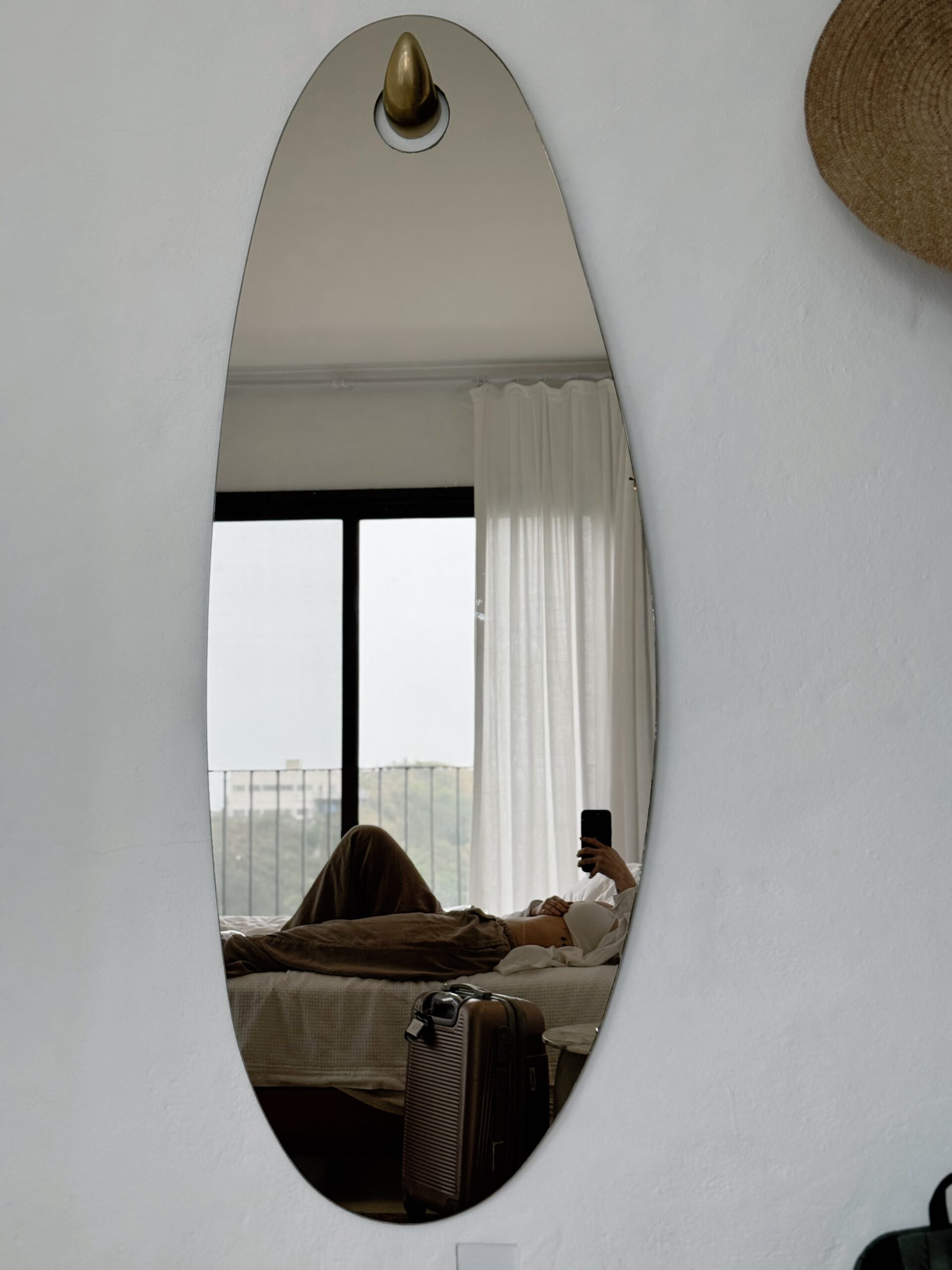 A woman resting on a bed reflected in a mirror with a suitcase nearby, representing a slow living reset, motherhood transitions, and vision-led planning for 2026.